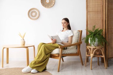 Evdeki rahat koltukta kitap okuyan güzel bir kadın.