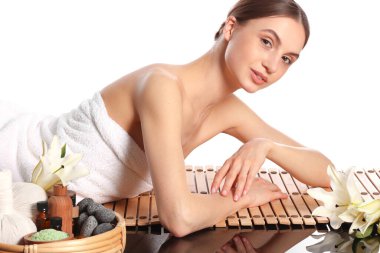 Beyaz arka planda bambu hasırında poz veren güzel bir kadın. Ayna yüzeyinde kaplıca ürünleri ve çiçekler