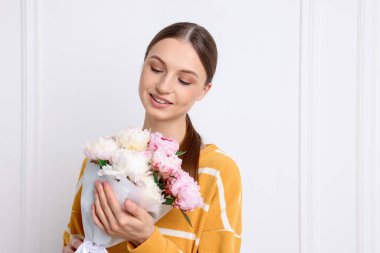 Beyaz duvarın yanında şakayık demeti olan güzel bir kadın.