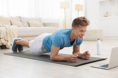 Evdeki koçla çevrimiçi derste tahta egzersizi yapan adam. Spor ve sağlıklı yaşam tarzı
