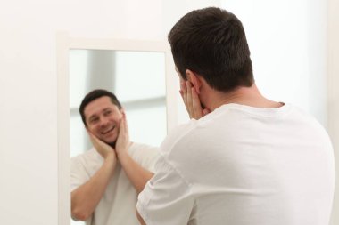 Yakışıklı adam aynada kendine bakıyor.