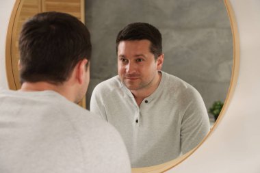 Yakışıklı adam aynada kendine bakıyor.