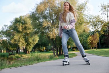Mutlu genç kadın paten kayıyor parkta, alçak açılı.