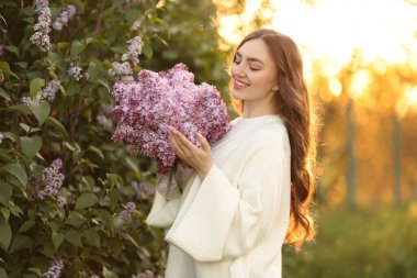 Gülümseyen kadın sabah çalıların yanında bir demet leylak çiçeğiyle