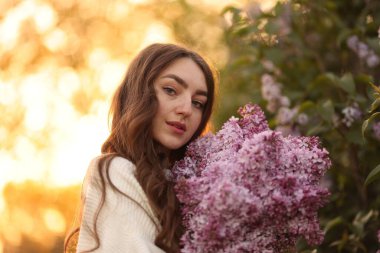 Güzel bir kadın portresi ve açık havada leylak çiçekleri.