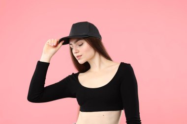 Pembe arka planda şık beysbol şapkalı güzel bir kadın.