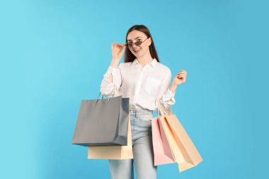 Açık mavi arka planda alışveriş torbaları olan pozitif kadın.