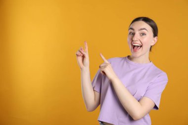 Şaşırmış bir kadın turuncu arka planda bir şeye işaret ediyor, mesaj için boşluk.