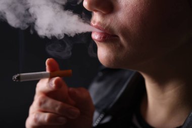 Siyah arka planda sigara içen kadın, yakın plan.