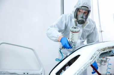 Kaportacıda sprey boyayla araba boyayan bir işçi. Metin için boşluk