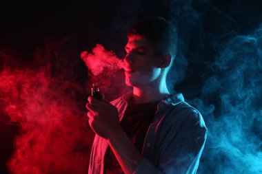 Koyu arkaplandaki neon ışıklarda elektronik sigara içen adam