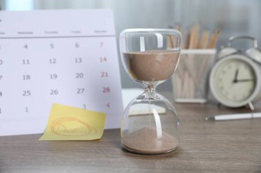 Kapalı masa üzerinde son teslim tarihi, kum saati, takvim, kırtasiye ve alarm saati olan yapışkan bir not.