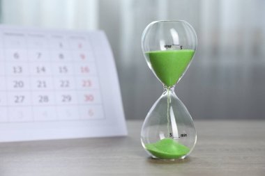 Son teslim tarihi. Kapalı alanda ahşap masada kum ve takvim akan kum saati.