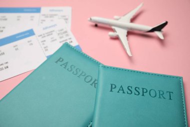 Biletli pasaportlar ve pembe arka planda uçak modeli, yakın plan.