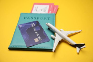 Biletli pasaport, kredi kartı ve sarı arka planda uçak modeli, yakın plan.