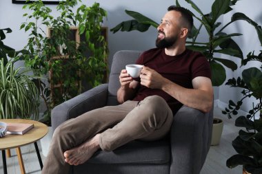 Uyum. Evdeki koltukta içki içen adam.