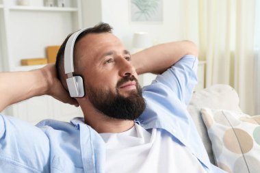 Uyum. Evdeki koltukta kulaklıkla müzik dinleyen bir adam.