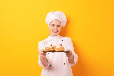 Üniformalı şekerci turuncu arka planda lezzetli profiteroller tutuyor.