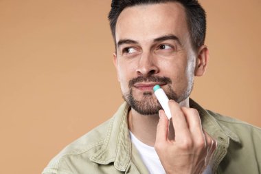 Yakışıklı bir adam açık kahverengi arka planda dudaklarına merhem sürüyor.