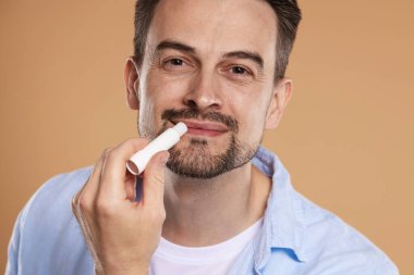 Yakışıklı bir adam açık kahverengi arka planda dudaklarına merhem sürüyor.
