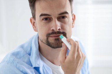 Bulanık ışık arka planında dudaklarına dudak kremi süren yakışıklı bir adam.