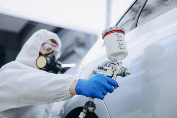 Worker painting car in body shop, selective focus