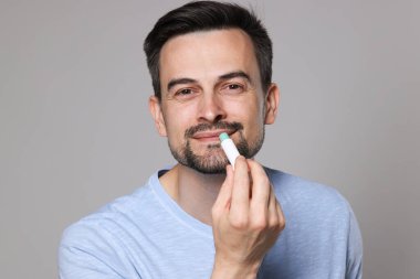 Gri arka planda dudaklarına dudak kremi süren yakışıklı bir adam.