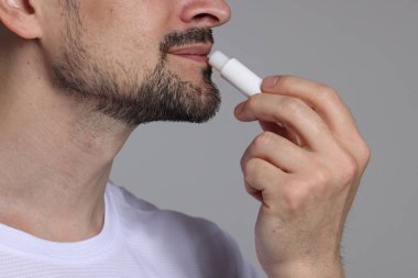 Gri arka planda dudaklarına merhem süren adam, yakın plan.