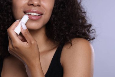 Gülümseyen kadın gri arka planda dudaklarına merhem sürüyor.