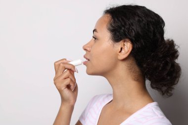 Gri arka planda dudaklarına merhem süren güzel bir kadın.