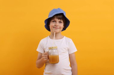 Panama şapkalı, turuncu arka planda meyve suyu kavanozu olan şirin bir çocuk. Tazeleyici içecek.
