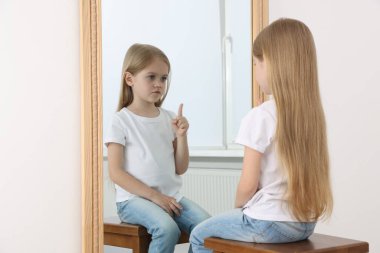 Üzgün küçük kız aynada kendine bakıyor.