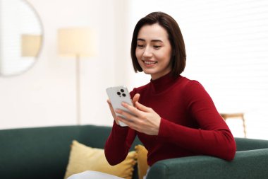 Evdeki koltukta modern akıllı telefon kullanan bir kadın. Metin için boşluk