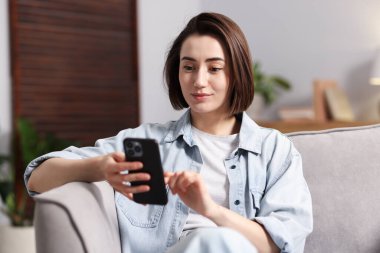 Evdeki koltukta modern akıllı telefon kullanan bir kadın.