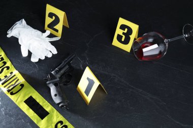 Adli tıp uzmanı. Sarı suç mahalli bandı, işaretler, silah, şarap ve eldivenler siyah masanın üstünde. Metin için boşluk