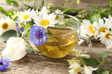 Cam bardakta Aromatik bitki çayı ve ahşap masada çiçekler, yakın plan.