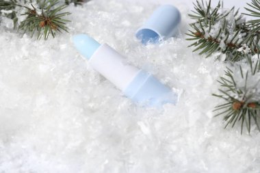 Nemlendirici dudak kremi ve suni kar üzerinde köknar ağacı dalları, yakın plan. Kış bakımı