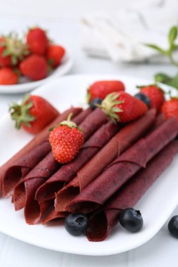 Lezzetli meyve dürümleri, çilekler ve yaban mersinleri beyaz masada, yakın plan.