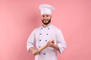 Üniformalı mutlu pastacı pembe arka planda raptiye tutuyor.