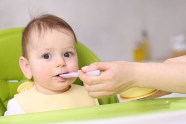 Anne bebeğini sandalyeyle besliyor, yakın plan.