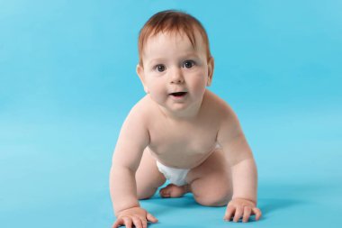 Açık mavi arka planda emekleyen şirin bir bebek.