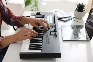 Beyaz masada MIDI klavyesiyle çalışan adam, yakın plan.