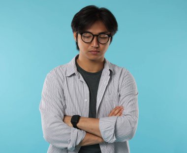 Açık mavi arka planda çapraz kollu gözlüklü yakışıklı Asyalı adam.