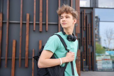 Dışarıdaki binanın yanında kulaklığı ve sırt çantası olan genç bir çocuk.