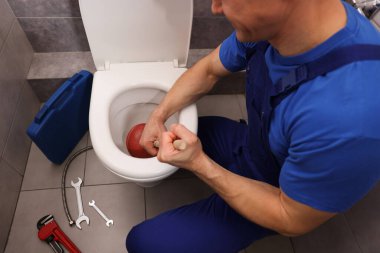 Tesisatçı tuvalet tıkanıklığını açıyor, içeride pompa var, yakın plan.