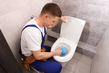 Tesisatçı içeride pompayla tuvaletin tıkanmasını açıyor.