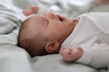 Sevimli yeni doğmuş bebek yatakta esniyor, yakın plan.