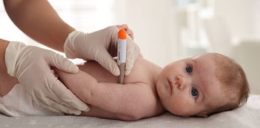 Klinikteki masada termometreyle bebeği muayene eden çocuk doktoru.