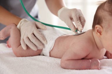 Klinikteki masada steteskopla bebeği muayene eden çocuk doktoru.