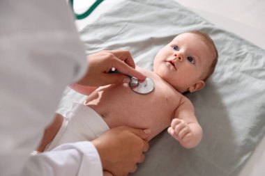 Klinikteki masada steteskopla bebeği muayene eden çocuk doktoru.